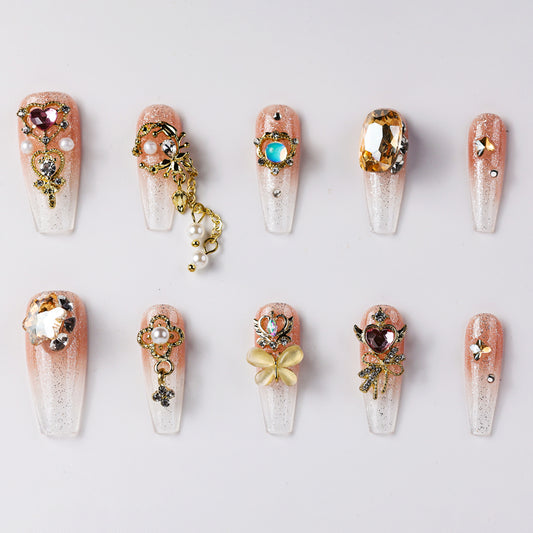 Elegant press-on nails featuring soft gradient peach and white designs, embellished with gold accents, rhinestones, pearls, and floral patterns. Includes luxurious butterfly and heart-shaped charms for a sophisticated look.